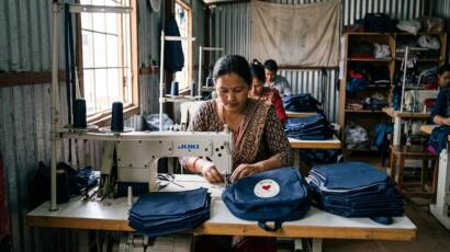 Anbringung von Schnallen an blauem Stoff für 255 Schulrucksäcke für Flutopfer Kinder in Nuwakot
