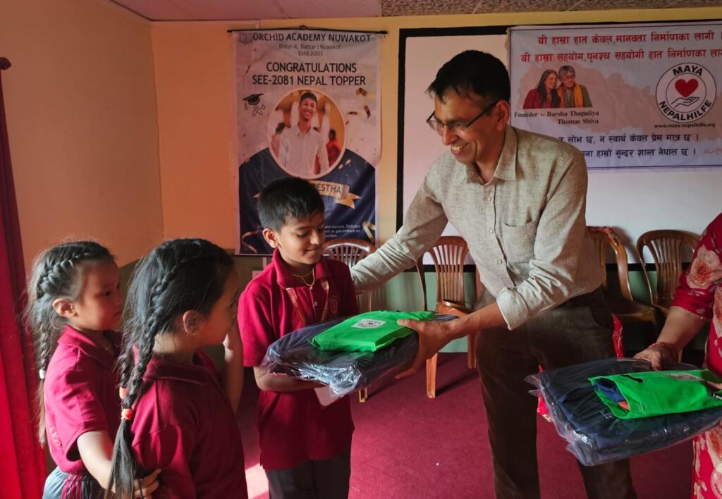 Vertreter der Maya Nepalhilfe übergibt am 9.10.26 ein Paket mit eigens angefertigtem wasserdichten Schulrucksack inklusive Federmäppchen und Pullover an Schülerinnen der Orchid Academy Nuwakot.